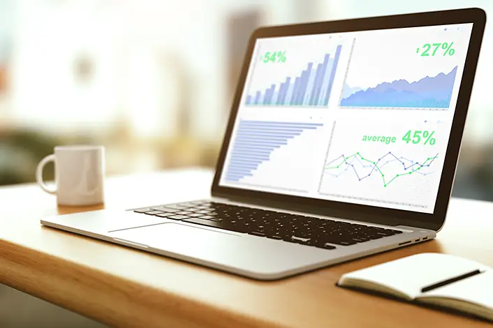 An open laptop on a desk with coffee and a notebook